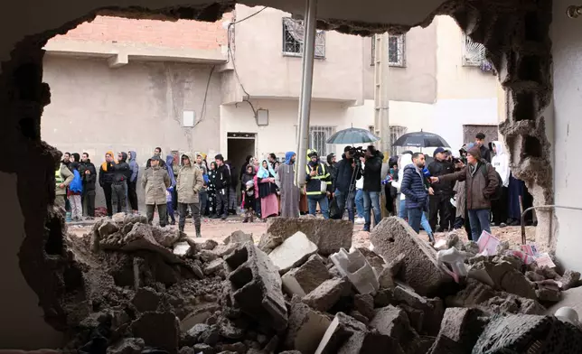 Residents and jounalists watch as rescue workers search for survivors, amid the wreckage of two collapsed buildings, in Fez, Morocco, Wednesday, Dec. 10, 2025. (AP Photo/Hanane Boukili)
