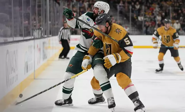 Minnesota Wild defenseman Jake Middleton, left, and Vegas Golden Knights defenseman Jeremy Lauzon battle for the puck during the first period of an NHL hockey game Monday, Dec. 29, 2025, in Las Vegas. (AP Photo/John Locher)