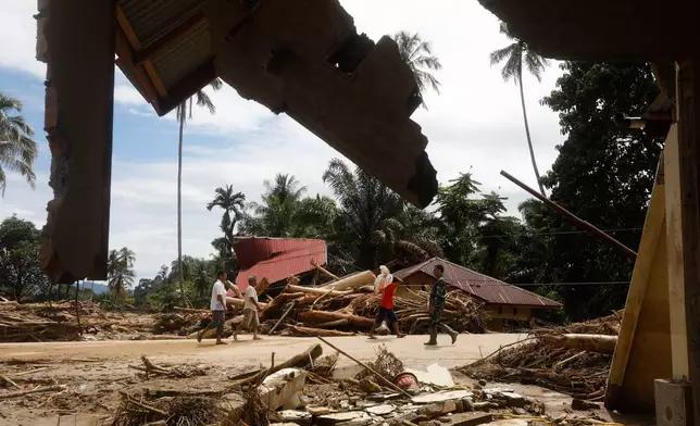 People walk past the ruins of houses at a village affected by flood in Batang Toru, North Sumatra, Indonesia, Wednesday, Dec. 3, 2025. (AP Photo/Binsar Bakkara)