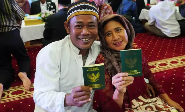 Suryadi, left, who uses only one name, and his bride Laili Nofiana show their wedding certificates after getting married in a mass wedding ceremony at Istiqlal Mosque in Jakarta, Indonesia, Wednesday, Dec. 3, 2025. (AP Photo/Tatan Syuflana)