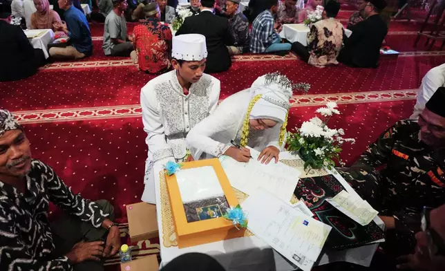 A bride signs her wedding certificate as the groom looks on during a mass wedding ceremony at Istiqlal Mosque in Jakarta, Indonesia, Wednesday, Dec. 3, 2025. (AP Photo/Tatan Syuflana)