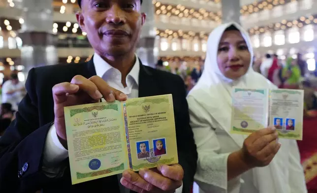 A bride and groom show their wedding certificates after getting married in a mass wedding ceremony at Istiqlal Mosque in Jakarta, Indonesia, Wednesday, Dec. 3, 2025. (AP Photo/Tatan Syuflana)