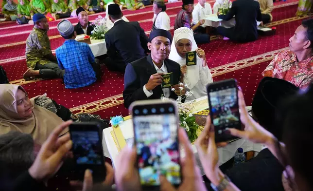 A bride and groom show their wedding certificates after getting married as family members use their mobile phones to take photos during a mass wedding ceremony at Istiqlal Mosque in Jakarta, Indonesia, Wednesday, Dec. 3, 2025. (AP Photo/Tatan Syuflana)