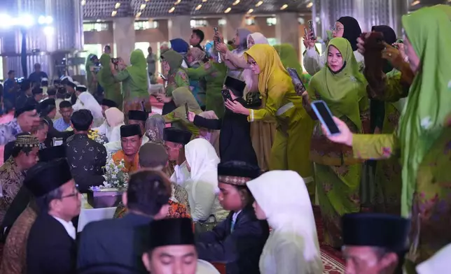 Family members use their phones to take photos during a mass wedding ceremony at Istiqlal Mosque in Jakarta, Indonesia, Wednesday, Dec. 3, 2025. (AP Photo/Tatan Syuflana)