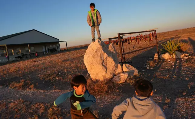 Young members of the Mayflower Church community play outside near pork belly strips curing on a pole to make a traditional Chinese bacon known as là ròu, in Midland, Texas, Jan. 18, 2025. (AP Photo/Rebecca Blackwell)
