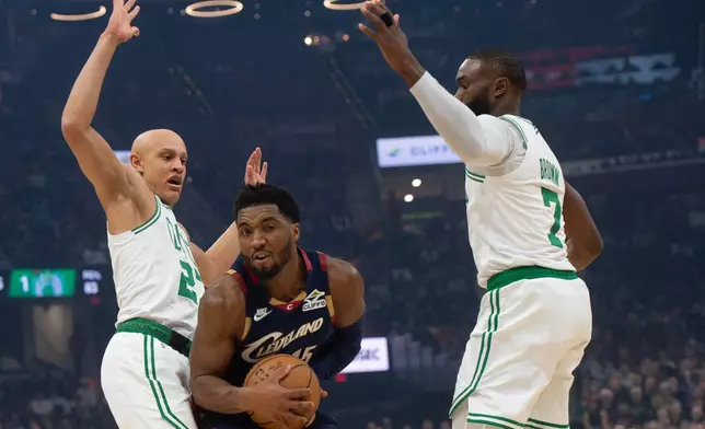 Cleveland Cavaliers' Donovan Mitchell, center, is guarded by Boston Celtics' Jordan Walsh, left, and Jaylen Brown during the first half of an NBA basketball game in Cleveland, Sunday, Nov. 30, 2025. (AP Photo/Phil Long)