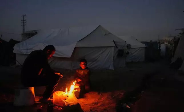 Displaced Palestinian Salah al-Mabhouh, 40, sits by the fire with his son Abdul-Razzaq 8, next to their tent in al-Bureij camp, central Gaza Strip, Wednesday, Dec. 24, 2025. (AP Photo/Abdel Kareem Hana)