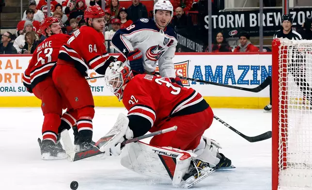 Columbus Blue Jackets' Zach Werenski (8) watches his shot bounce off Carolina Hurricanes goaltender Brandon Bussi (32) while being guarded by Carolina Hurricanes' Joel Nystrom (64) and Jackson Blake (53) during the third period of an NHL hockey game in Raleigh, N.C., Tuesday, Dec. 9, 2025. (AP Photo/Karl DeBlaker)