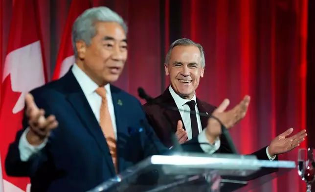 Prime Minister Mark Carney reacts as Michael Ma, Member of Parliament for Markham-Unionville, who crossed the floor from the Conservatives to the Liberals hours earlier, makes brief remarks at the Liberal caucus holiday party in Ottawa, on Thursday, Dec. 11, 2025. (Justin Tang/The Canadian Press via AP)