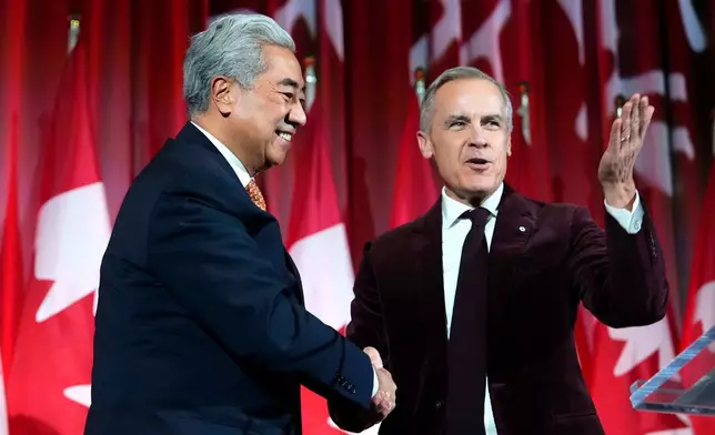 Canadian Prime Minister Mark Carney, right, shakes hands with Michael Ma, Member of Parliament for Markham-Unionville, who crossed the floor from the Conservatives to the Liberals hours earlier, as he brings him on stage at the Liberal caucus holiday party in Ottawa, Ontario, Thursday, Dec. 11, 2025. (Justin Tang/The Canadian Press via AP)