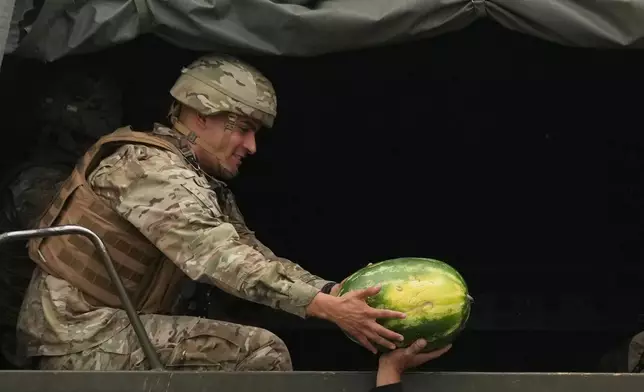 A watermelon vendor offers one to soldiers riding on a truck assigned to secure the presidential runoff election in Santiago, Chile, Sunday, Dec. 14, 2025. (AP Photo/Esteban Felix)