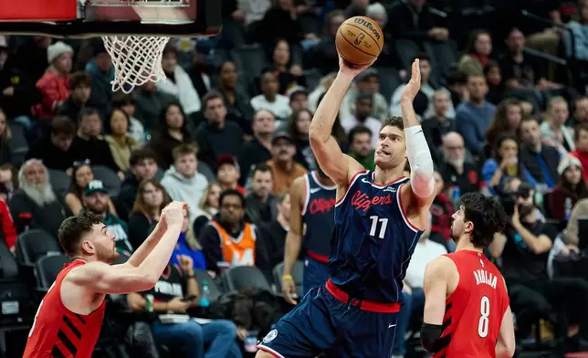 Los Angeles Clippers center Brook Lopez, center, shoots between Portland Trail Blazers center Donovan Clingan, left, and forward Deni Avdija during the second half of an NBA basketball game in Portland, Ore., Friday, Dec. 26, 2025. (AP Photo/Craig Mitchelldyer)
