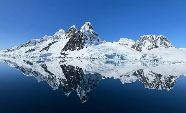 An ice covered rock formation is reflected in the waters at Pleneau Island in Antarctica, Monday, Nov. 24, 2025. (AP Photo/Mark Baker)