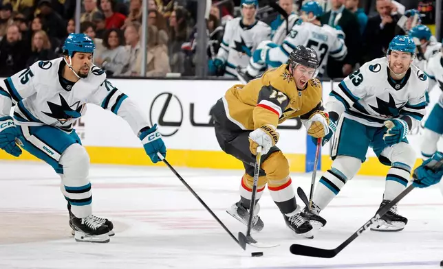 Vegas Golden Knights defenseman Ben Hutton (17) reaches for the puck between San Jose Sharks right wing Ryan Reaves (75) and center Barclay Goodrow (23) during the second period of an NHL hockey game Tuesday, Dec. 23, 2025, in Las Vegas. (AP Photo/Steve Marcus)