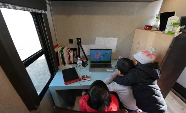 Siblings Mo Songhua, left, Mo Songen, center, and Mo Nika, right, from the Mayflower Church community watch, "Peppa Pig," to strengthen their English, inside their family's trailer in Midland, Texas, Jan. 20, 2025. (AP Photo/Rebecca Blackwell)