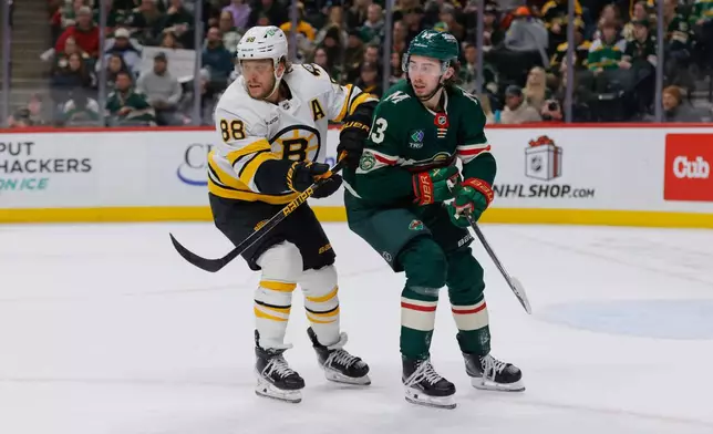Minnesota Wild defenseman Quinn Hughes, right, and Boston Bruins right wing David Pastrnak (88) battle for position during the first period of an NHL hockey game, Sunday, Dec. 14, 2025, in St. Paul, Minn. (AP Photo/Bailey Hillesheim)