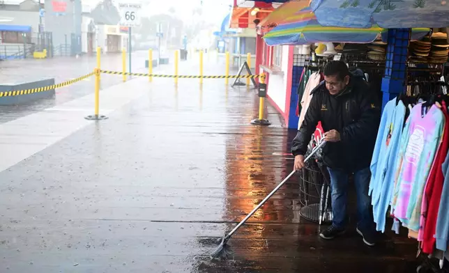 Miguel Lopez sweeps water from Marlene's Beachcomber on the Santa Monica pier Wednesday, Dec. 24, 2025, in Santa Monica, Calif. (AP Photo/Wally Skalij)