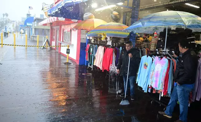 Miguel Lopez sweeps water from Marlene's Beachcomber on the Santa Monica pier Wednesday, Dec. 24, 2025, in Santa Monica, Calif. (AP Photo/Wally Skalij)