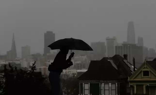 A pedestrian carries an umbrella while walking on a path at Alamo Square Park, in San Francisco, Tuesday, Dec. 23, 2025. (AP Photo/Jeff Chiu)