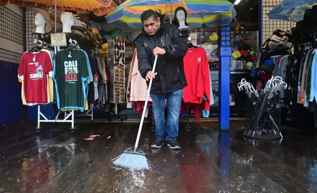 Miguel Lopez sweeps water from Marlene's Beachcomber on the Santa Monica pier Wednesday, Dec. 24, 2025, in Santa Monica, Calif. (AP Photo/Wally Skalij)