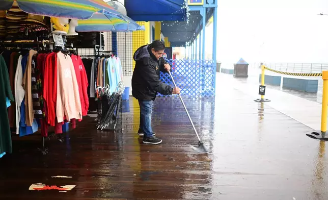 Miguel Lopez sweeps water from Marlene's Beachcomber on the Santa Monica pier Wednesday, Dec. 24, 2025, in Santa Monica, Calif. (AP Photo/Wally Skalij)