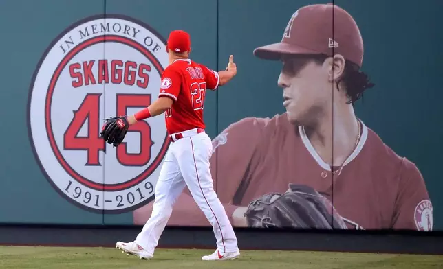 FILE - Los Angeles Angels center fielder Mike Trout gestures toward a photo of Tyler Skaggs in center field prior to a baseball game against the Detroit Tigers in Anaheim, Calif., on July 29, 2019. (AP Photo/Mark J. Terrill, File)