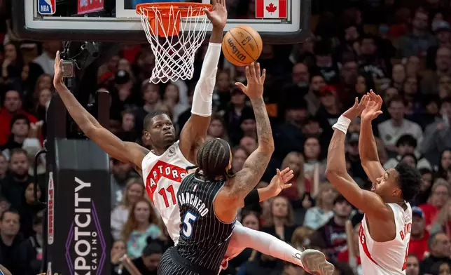 Toronto Raptors center Mo Bamba (11) and forward Scottie Barnes, right, defend against Orlando Magic forward Paolo Banchero (5) as he shoots during first half NBA action in Toronto on Monday Dec. 29, 2025. THE (Frank Gunn/The Canadian Press via AP)