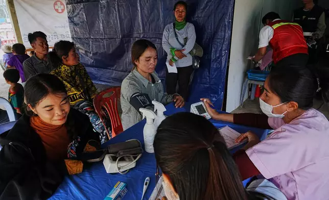 Evacuated people, left, receive medical check up as they take refuge at Batthkoa primary school in Oddar Meanchey province, Cambodia Wednesday, Dec. 10, 2025, after fleeing homes following a fighting between Thailand and Cambodia over territorial claims. (AP Photo/Heng Sinith)