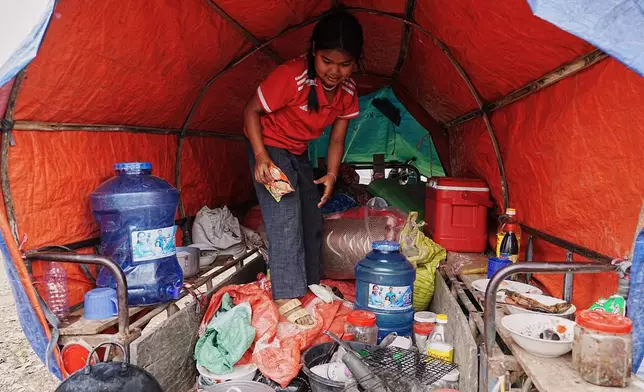 An evacuated young girl collects food in a tent as she takes refuge in Batthkoa primary school in Oddar Meanchey province, Cambodia, Wednesday, Dec. 10, 2025, after fleeing home following a fighting between Thailand and Cambodia over territorial claims. (AP Photo/Heng Sinith)