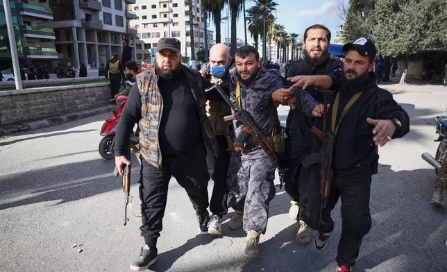A police officer injured by a thrown stone is helped away from the area after clashes erupted between Alawite protesters from the Alawite religious minority and counterprotesters, two days after a bomb in an Alawite mosque in Homs killed eight people and wounded 18 during Friday prayers, in Latakia, Syria's coastal region, Sunday, Dec. 28, 2025. (AP Photo/Omar Albam)