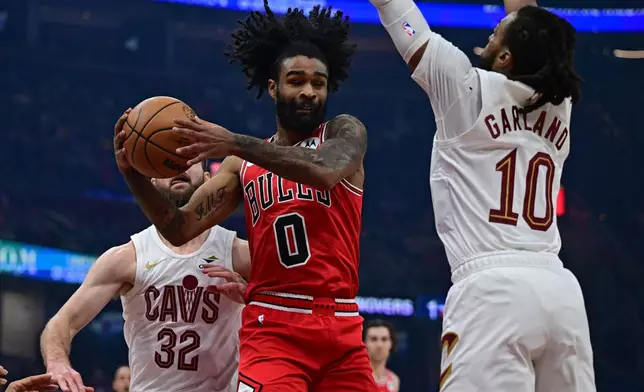 Chicago Bulls guard Coby White goes to the basket between Cleveland Cavaliers guard Darius Garland, right, and forward Dean Wade in the first half of an NBA basketball game, Friday, Dec. 19, 2025, in Cleveland. (AP Photo/David Dermer)