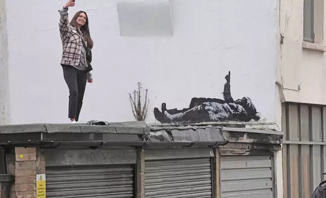 A person takes a selfie of a piece of graffiti artwork depicting two children, in London, Monday, Dec. 22, 2025 as elusive street artist Banksy appeared to confirm Monday that a new mural in London, depicting two children lying down and pointing up at the sky, is his latest work. (Stefan Rousseau/PA via AP)