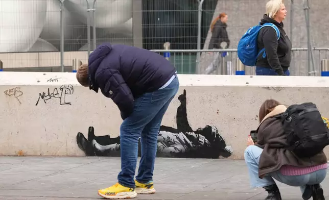 People take pictures of a graffiti artwork, depicting two people, outside Tottenham Court Road Station in London, Monday, Dec. 22, 2025 as elusive street artist Banksy appeared to confirm Monday that an identical image appeared on a wall on the side of a building in Bayswater, west London is his latest work. (AP Photo/Kirsty Wigglesworth)