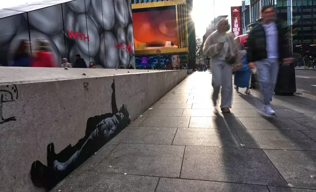 Pedestrians walk past a graffiti artwork, depicting two people, which recently appeared, outside Tottenham Court Road Station in London, Monday, Dec. 22, 2025 as elusive street artist Banksy appeared to confirm Monday that an identical image appeared on a wall on the side of a building in Bayswater, west London is his latest work. (AP Photo/Kirsty Wigglesworth)