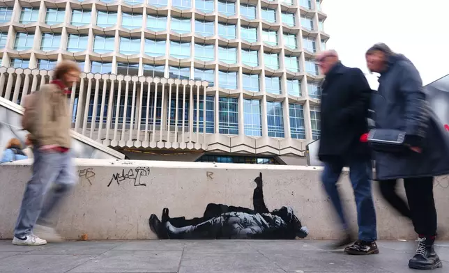 Pedestrians walk past a graffiti artwork, depicting two people, outside Tottenham Court Road Station in London, Monday, Dec. 22, 2025 as elusive street artist Banksy appeared to confirm Monday that an identical image appeared on a wall on the side of a building in Bayswater, west London is his latest work. (AP Photo/Kirsty Wigglesworth)