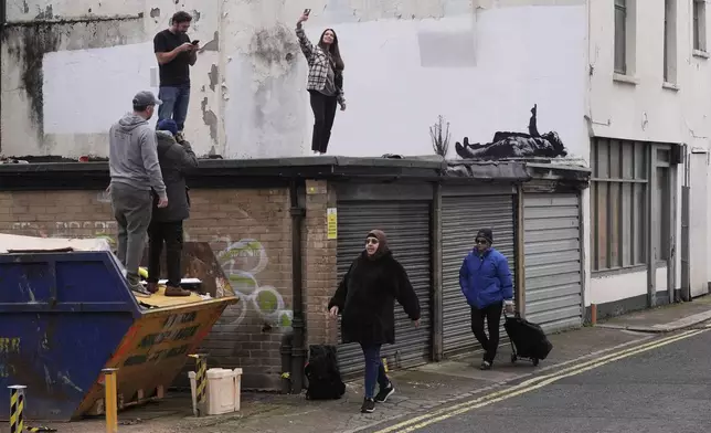 A person takes a selfie with a piece of graffiti artwork depicting two children, in London, Monday, Dec. 22, 2025 as elusive street artist Banksy appeared to confirm Monday that a new mural in London, depicting two children lying down and pointing up at the sky, is his latest work. (Stefan Rousseau/PA via AP)