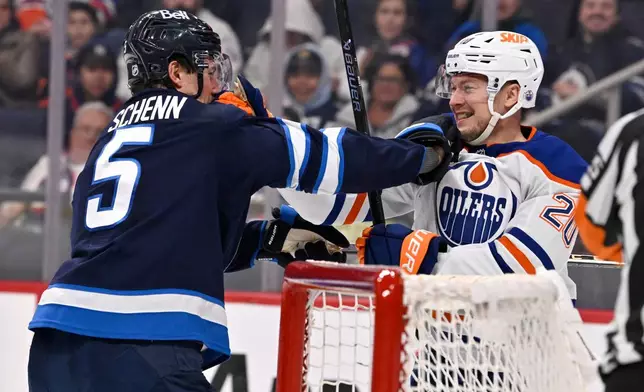 Edmonton Oilers' Curtis Lazar (20) and Winnipeg Jets' Luke Schenn (5) grab each other after a whistle during the first period of their NHL hockey game, in Winnipeg, Manitoba, Monday, Dec. 29, 2025. (Fred Greenslade/The Canadian Press via AP)