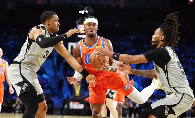 Oklahoma City Thunder guard Shai Gilgeous-Alexander, center, tangles with San Antonio Spurs' Keldon Johnson (3) and Stephon Castle (5) under the net in the first half of an NBA Cup semifinals basketball game, Saturday, Dec. 13, 2025, in Las Vegas. (AP Photo/Ronda Churchill)