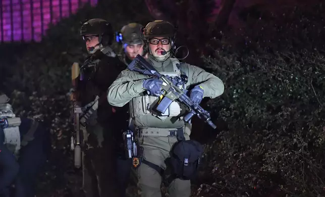 Law enforcement officials carry rifles on a street in a neighborhood near Brown University, Saturday, Dec. 13, 2025, in Providence, R.I. during the investigation of a shooting. (AP Photo/Steven Senne)