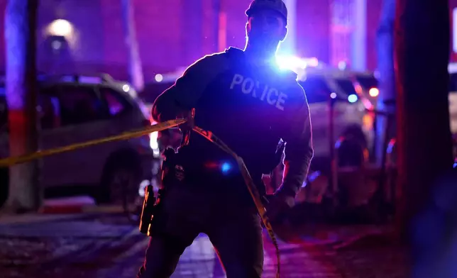 A police officer hangs yellow crime tape at Brown University in Providence, R.I., on Saturday, Dec. 13, 2025, during the investigation of a shooting. (AP Photo/Mark Stockwell)