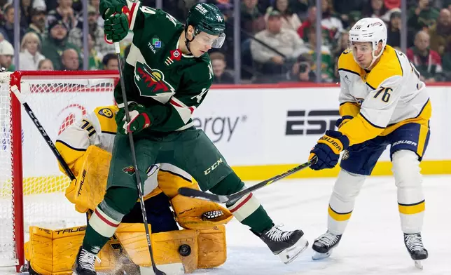 Minnesota Wild's Joel Eriksson Ek (14) tries to get the puck past Nashville Predators goalie Juuse Saros (74) as Predators's Brady Skjei (76) defends in the first period of an NHL hockey game against the Minnesota Wild, Tuesday, Dec. 23, 2025, in St. Paul, Minn. (Carlos Gonzalez/Star Tribune via AP)