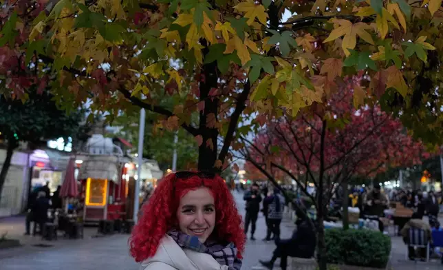 A woman smiles under a colourful tree in the northern city of Rasht, Iran, on Friday, Dec. 26, 2025. (AP Photo/Vahid Salemi)