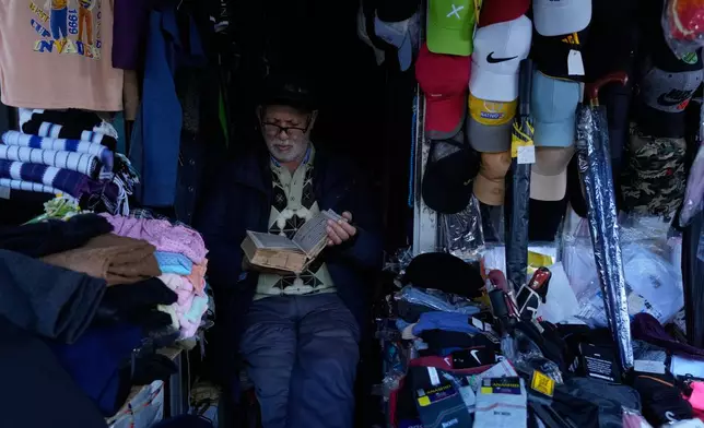 Ghesmat Masoumi reads the Quran at his shop in the port city of Bandar Anzali, Iran, Sunday, Dec. 21, 2025. (AP Photo/Vahid Salemi)