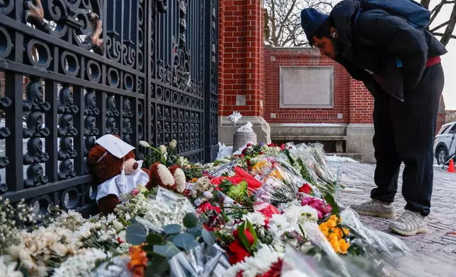 A community member looks at flowers, notes and mementos in a makeshift memorial display sitting in front of Brown University's Van Wickle gates, in Providence, R.I., two days after a shooting took place on the university's campus, Monday, Dec. 15, 2025. (Lily Speredelozzi/The Sun Chronicle via AP)