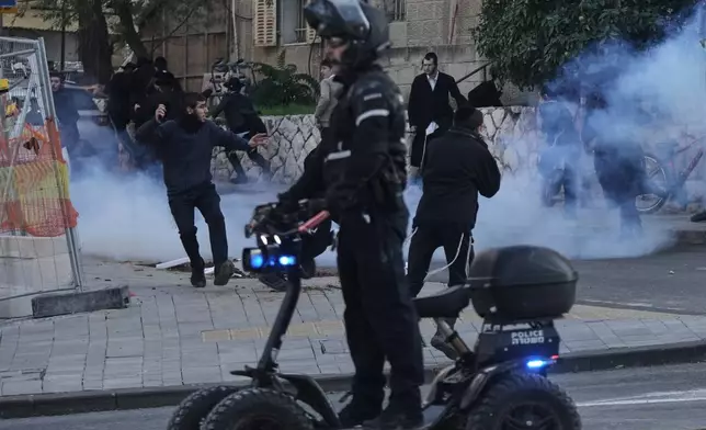 Ultra-Orthodox Jewish protesters run for cover from a gas grenade thrown by Israeli police during a violent disturbance in Jerusalem, Thursday, Dec. 18, 2025. (AP Photo/Mahmoud Illean)