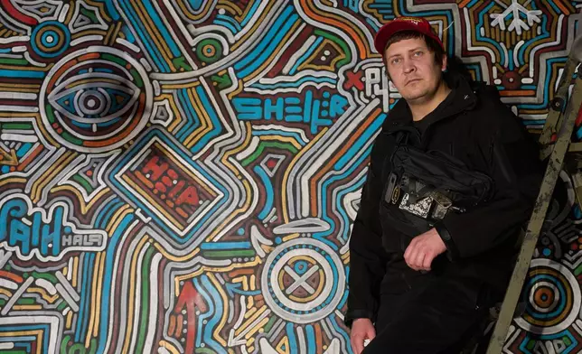 Ukrainian street artist Maxim Kilderov stands by his painting containing symbols and messages of resistance in his private museum that displays a collection of battlefield artifacts documenting Russia's invasion of Ukraine in Kyiv, Ukraine, Tuesday, Dec. 16, 2025. (AP Photo/Efrem Lukatsky)
