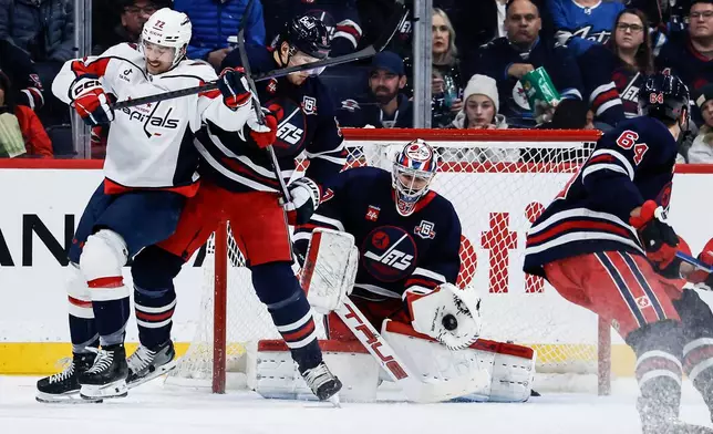 Winnipeg Jets goaltender Connor Hellebuyck (37) saves the shot as Luke Schenn (5) defends against Washington Capitals' Brandon Duhaime (left) during the second period of an NHL game in Winnipeg on Saturday, Dec. 13, 2025. (John Woods/The Canadian Press via AP)
