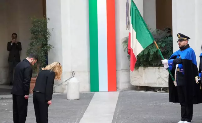 Ukraine's President Volodymyr Zelenskyy, left, and Italian Premier Giorgia Meloni pay their respects to the Italian flag at Chigi Palace, Tuesday, Dec. 9, 2025. (AP Photo/Gregorio Borgia)