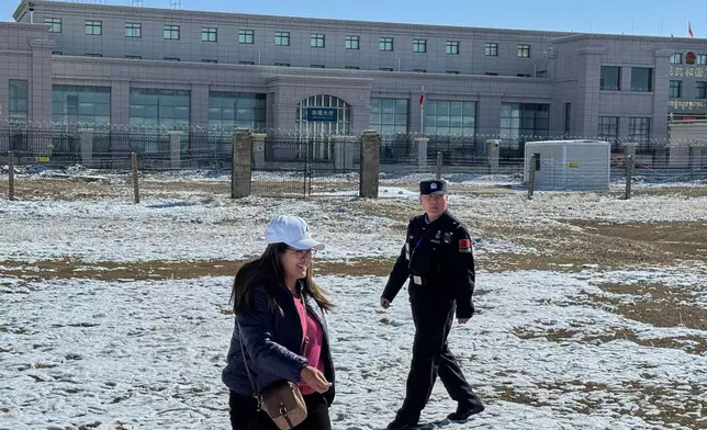 A Chinese police officer patrols near a Nepali tourist posing for a photograph at the Korola border between Nepal and China in Mustang district, Nepal, April 18, 2025. (AP Photo/Niranjan Shrestha)
