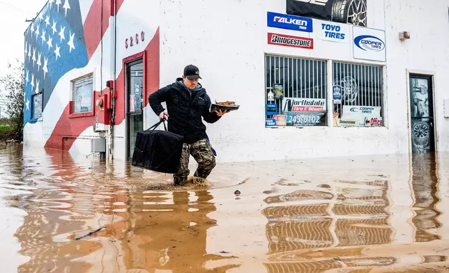 Dekoda Cruz walks through flood water while helping a friend who's tire shop flooded during heavy rains on Monday, Dec. 22, 2025, in Redding, Calif. (AP Photo/Noah Berger)